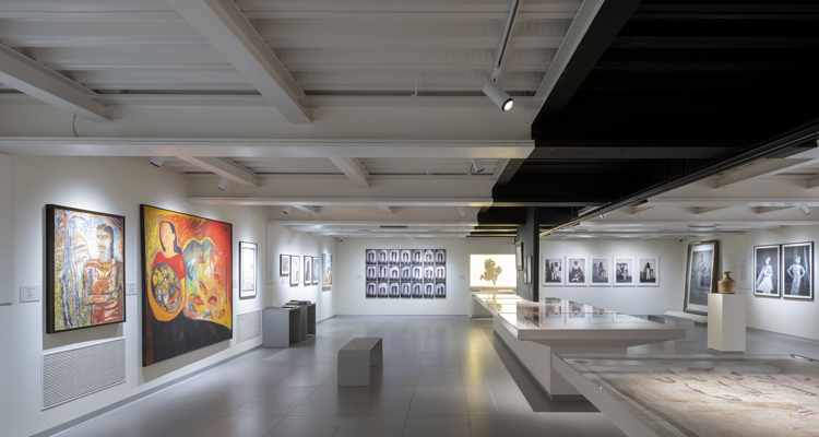 Interior view of a modern art gallery displaying paintings & photographs in a well-lit space.