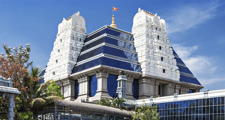 ISKCON Temple with stunning blue glass facade & white towers under a clear sky in Bangalore.