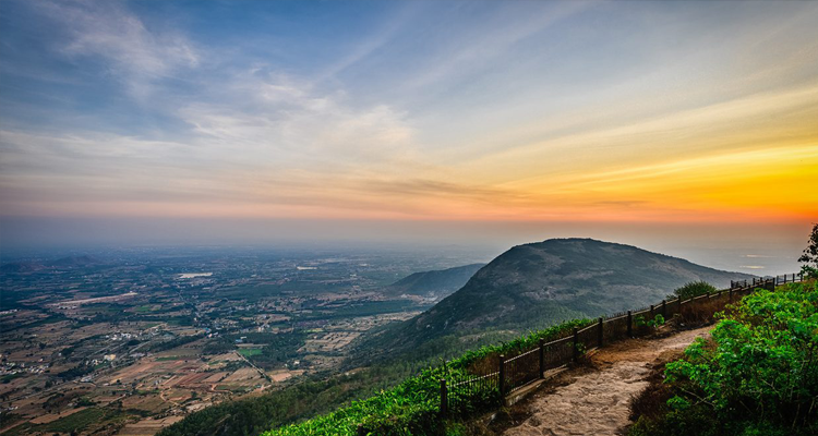 Nandi Hills landscape with a mountain peak, surrounded by clouds and framed by tree branches.