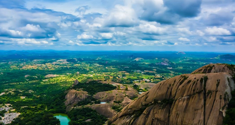 Stunning Savandurga Hill with rocky formations amidst verdant greenery under a vibrant sky.